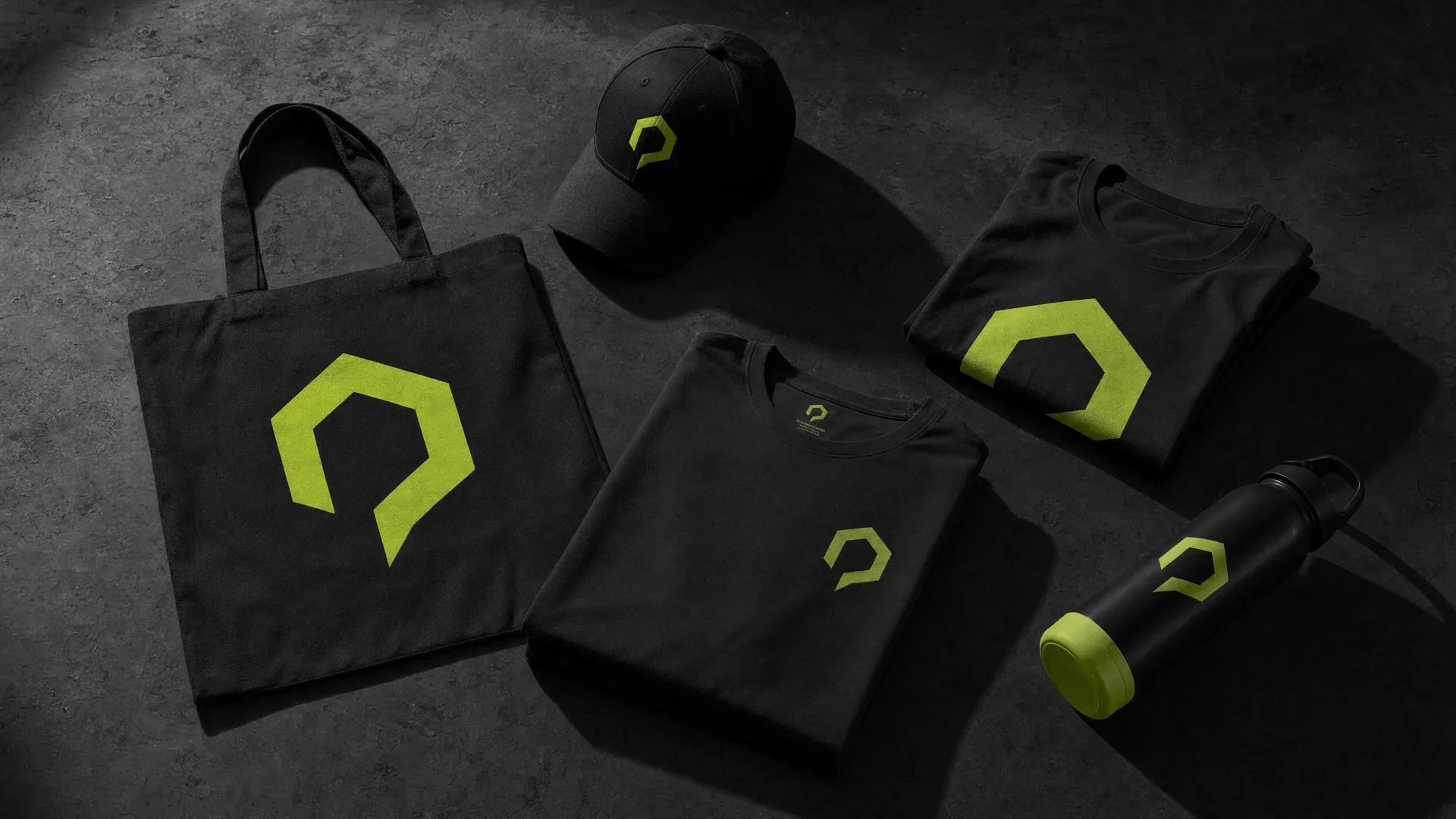 Black branded tote bags, caps and apparel with lime AdaptAd marks laid out on a dark surface
