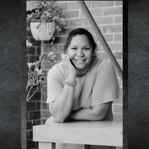 Marion Finch of AdaptAd smiling beside a brick wall, black and white portrait
